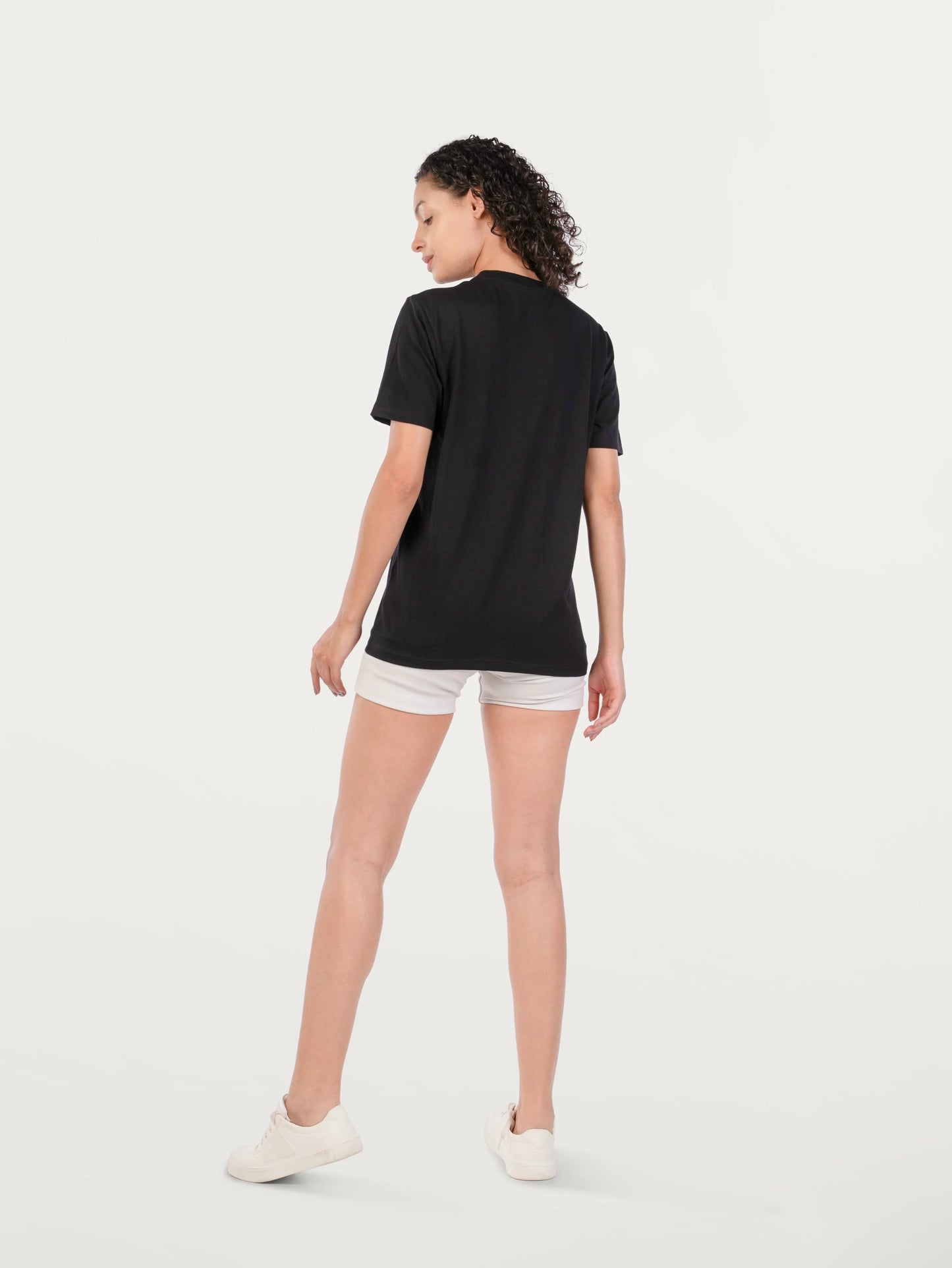 Woman wearing black t-shirt and white shorts, standing against plain white background