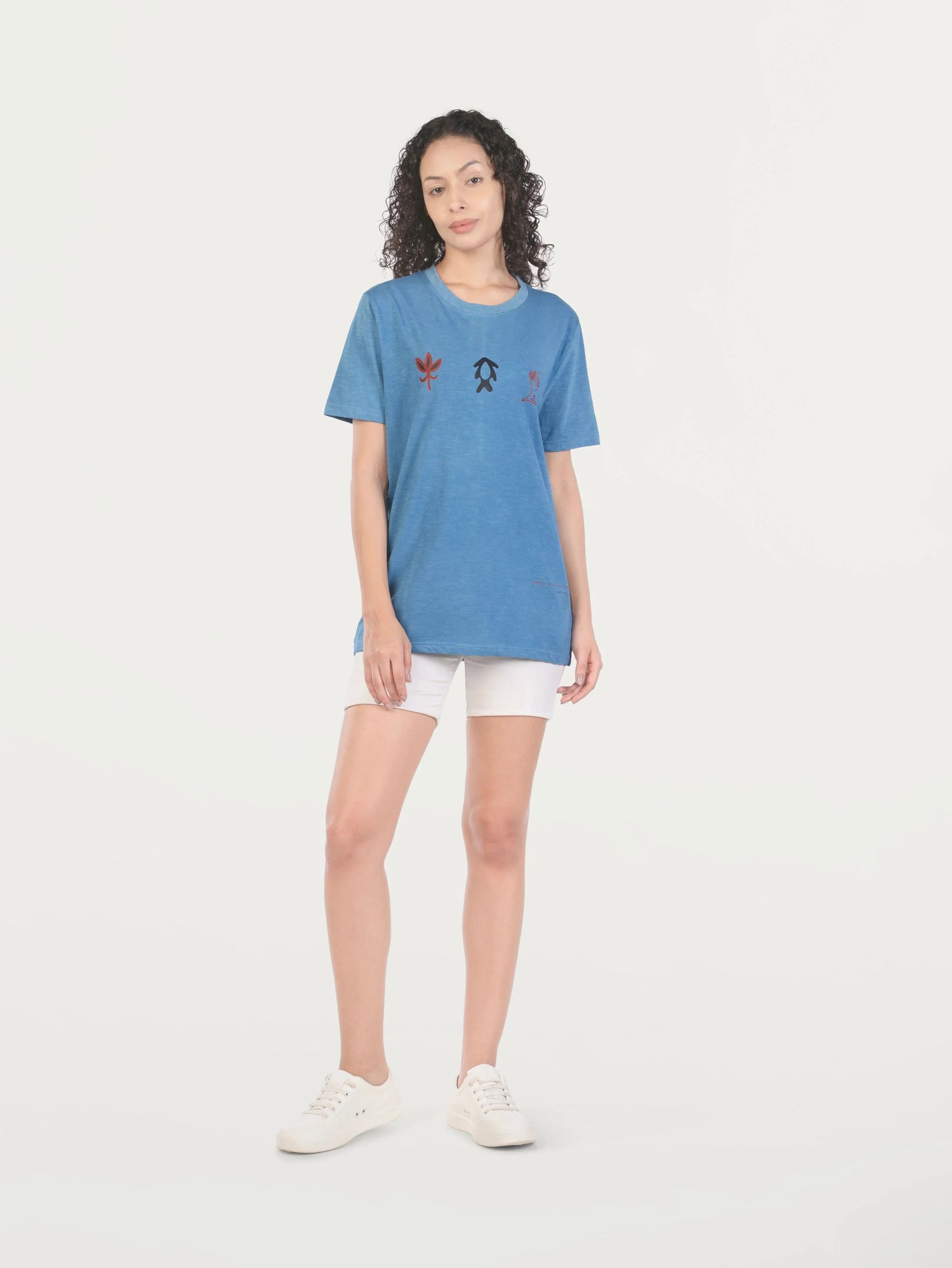 Woman wearing blue graphic t-shirt, white shorts, and white sneakers in studio setting