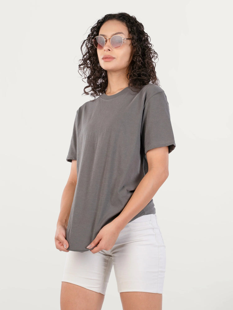 Woman with curly hair wearing round sunglasses, gray t-shirt, and white shorts on white background