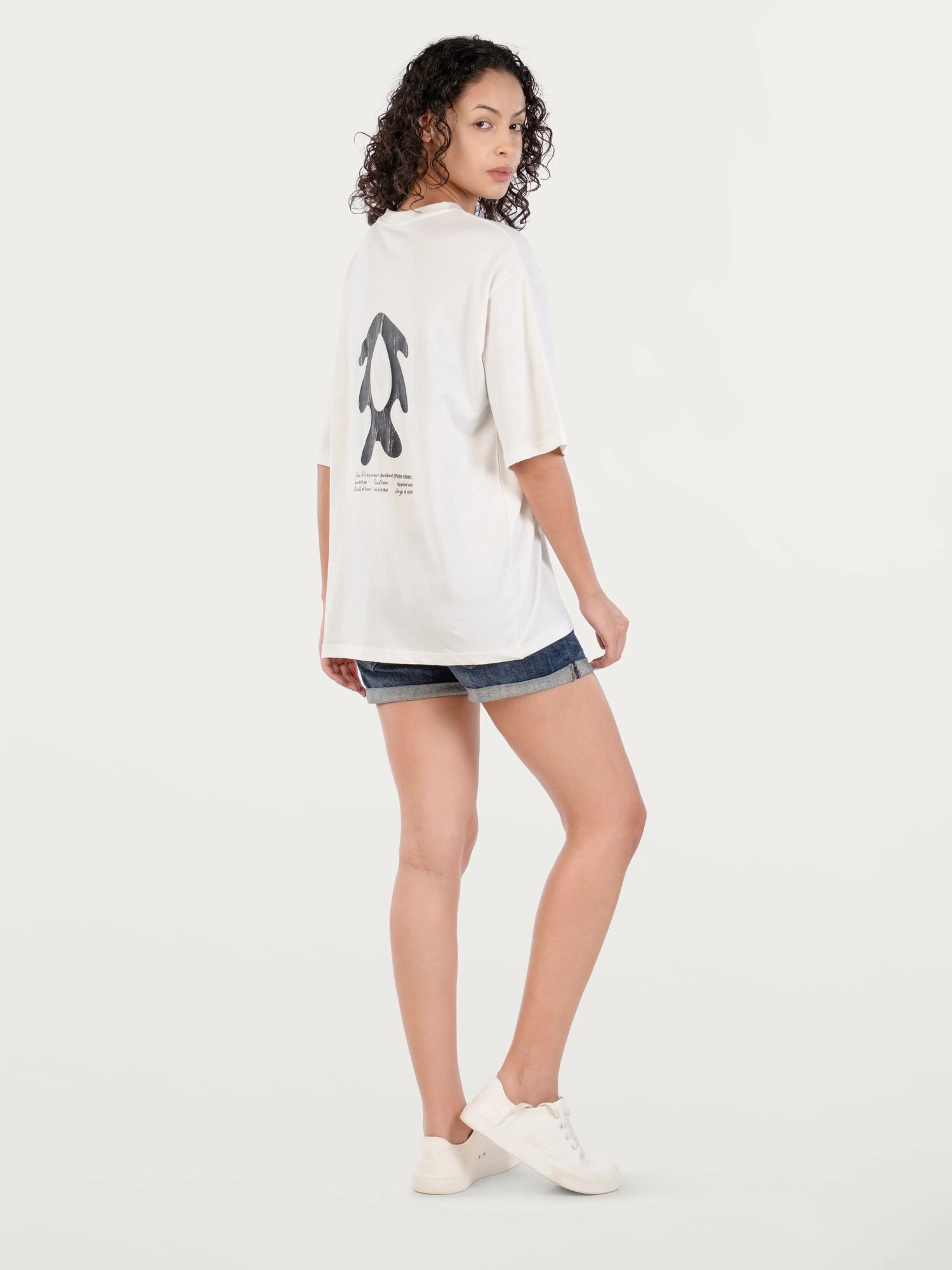 Woman wearing white graphic oversized t-shirt with black abstract design and denim shorts on white background