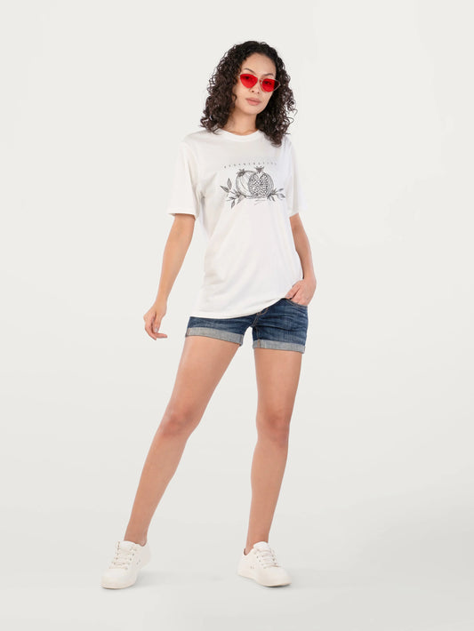 Woman wearing white graphic t-shirt with pomegranate design, denim shorts, red sunglasses, and white sneakers