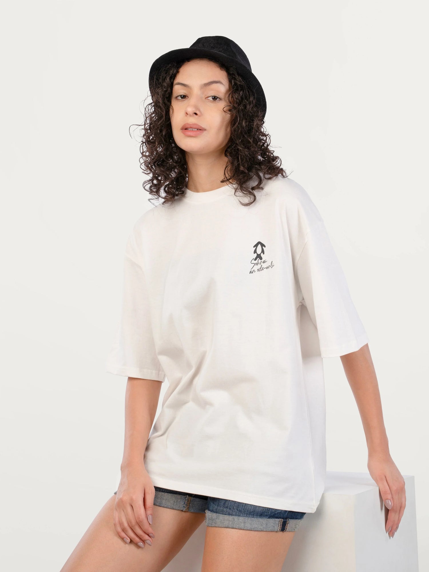 Young woman wearing a white oversized graphic t-shirt, denim shorts, and a black bucket hat